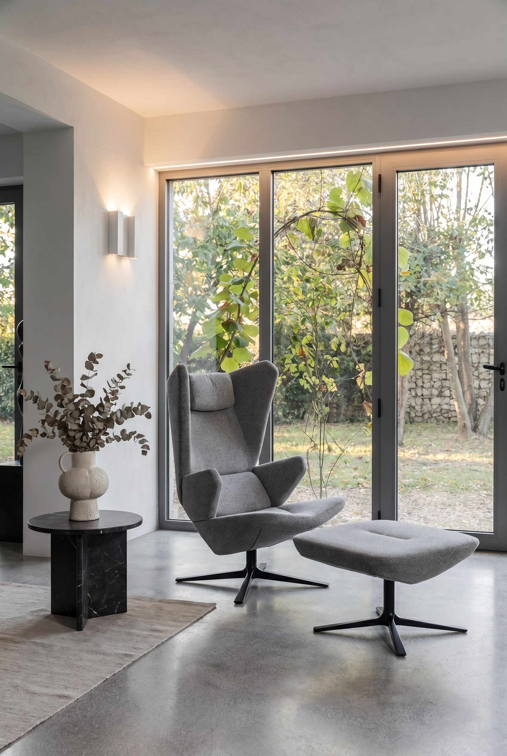 Modernes Wohnzimmer mit Sessel Trifidae in grauem Strukturstoff, Beistelltisch mit Keramikvase und großflächigen Fenstern