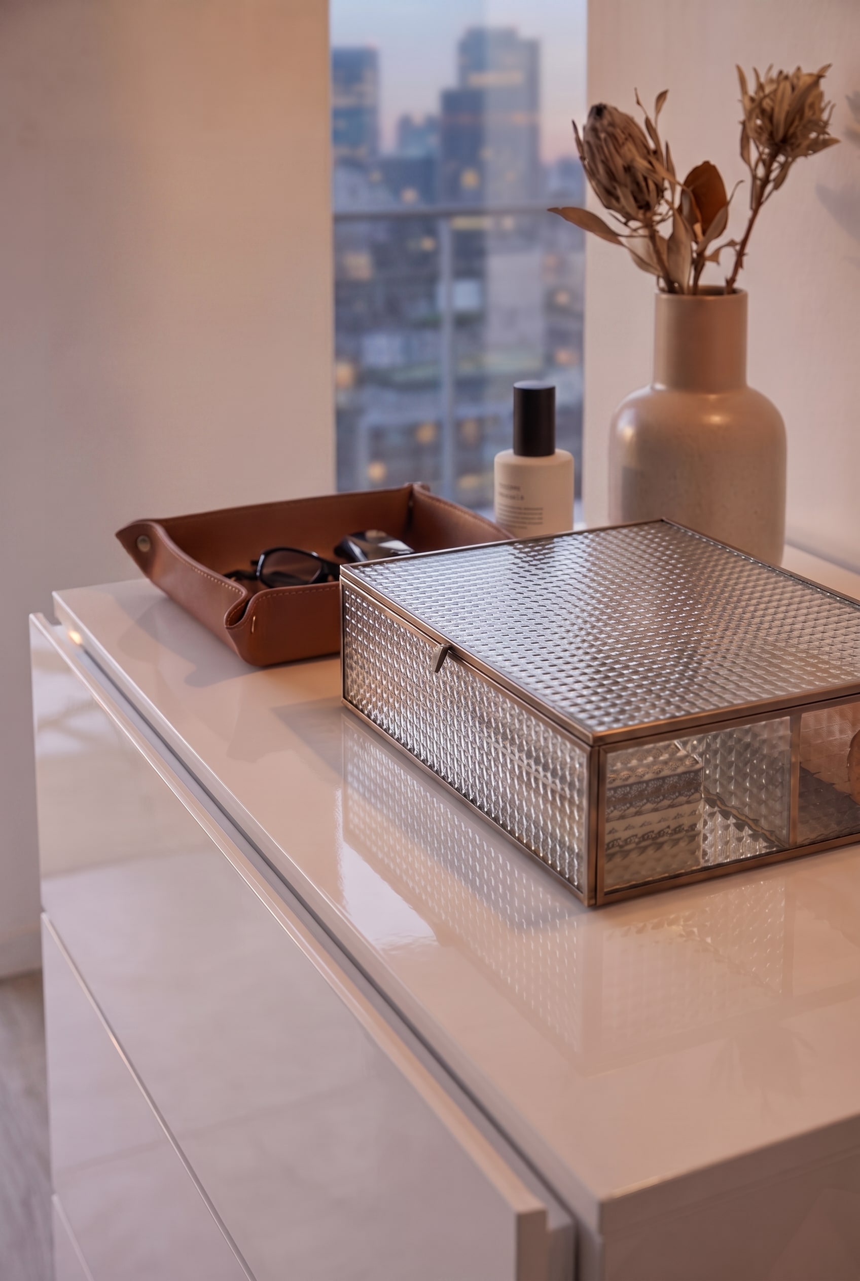 Draufsicht auf eine wei&szlig;e Hochglanzkommode mit Glasbox und Lederschale, puristisch ohne Garderobenstange inszeniert.