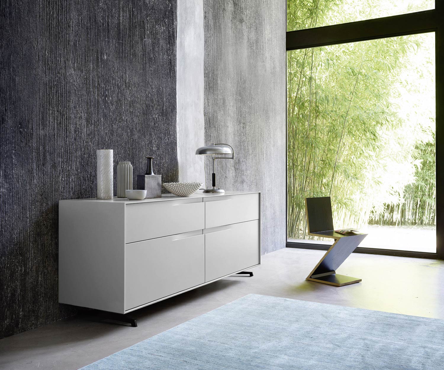 Commode design Vela laquée gris mat dans la chambre à coucher devant la baie vitrée Commode design Vela laquée gris mat dans la chambre à coucher devant la baie vitrée